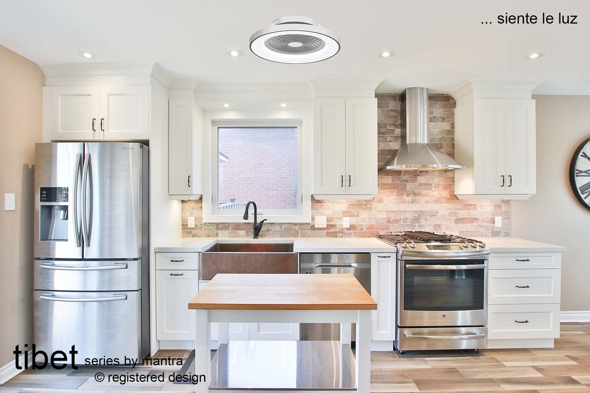 A modern kitchen featuring white cabinetry, stainless steel appliances including a French door refrigerator and a stove with a range hood, a central island with a wooden countertop, and tiled backsplash. The ceiling light is circular with "Tibet Silver Ceiling Fan by Ceiling Fans UK" text and is an LED dimmable ceiling light integrated with a 35W DC reversible fan, controllable via remote, app, or Alexa/Google Voice, and comes with a 5-year warranty.